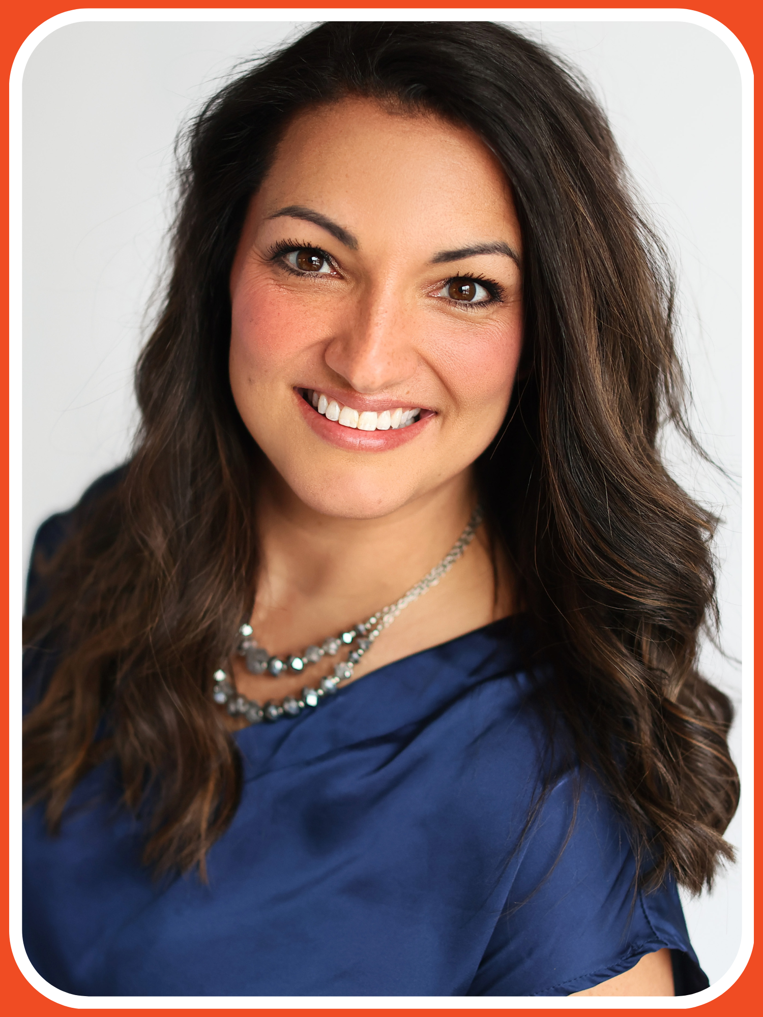 Close-up of a smiling woman with long dark hair, wearing a blue top and layered silver bead necklace.